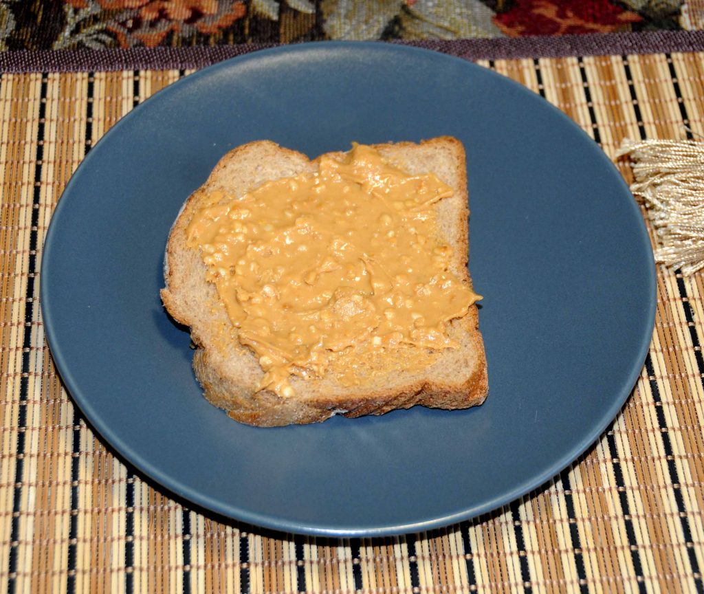 Μια φέτα ψωμί ολικής αλέσεως και μια κουταλιά του γλυκού φυστικοβούτυρο - A slice of whole grain bread and a spoonful of sweet peanut butter